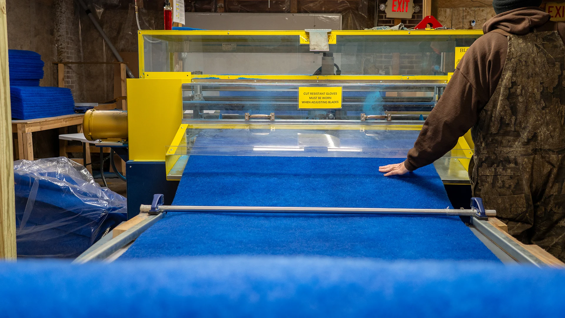 Worker feeding a roll of blue polyester filter media into a yellow industrial cutting machine in a production facility