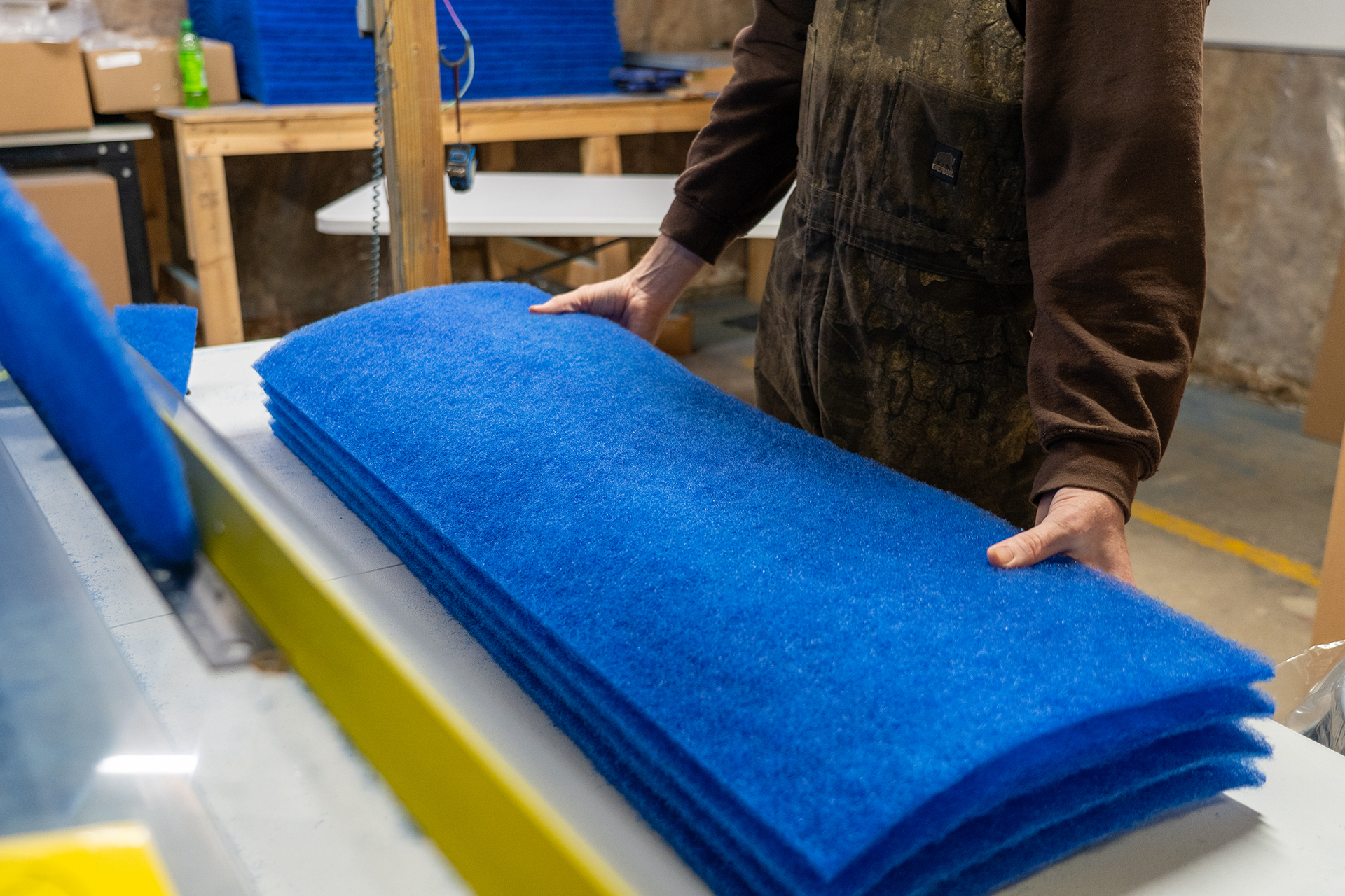 Worker handling stacked blue cut-to-size air filter pads on a production table