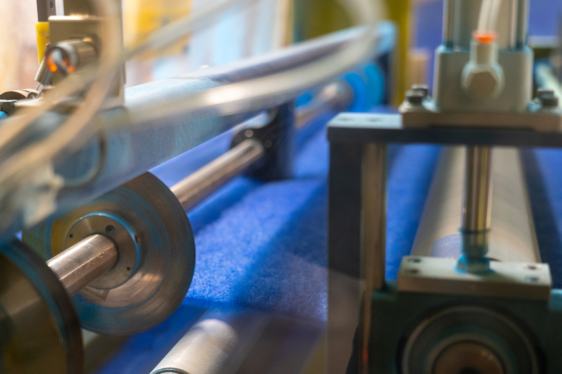 Close-up view of blue filter media moving through rollers inside a cutting machine